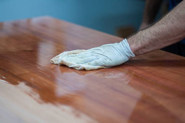 Finshing a timber table top by hand with oil or wax. French polishing wooden furniture with a rag to achieve a shiny, flawless surface. Taken in a woodworking workshop with a professional wood finisher. Fine woodwork.